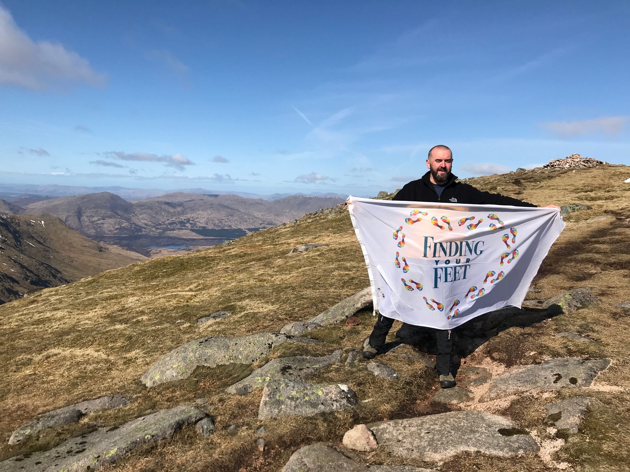 'MUNROFLAGGER: Bobby unfurls his Finding Your Feet flag on Beinn Eunaich while still keeping his distance from the cairn'